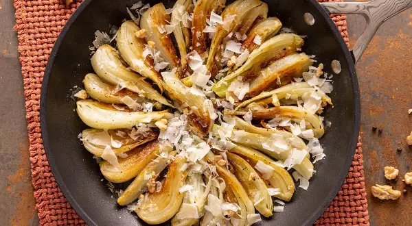 Finocchi in padella dorati e caramellati, guarniti con scaglie di formaggio e noci croccanti. Un piatto semplice e gustoso.