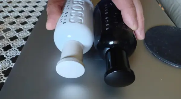 Dwie butelki perfum Hugo Boss, jedna biała męska, druga czarna, leżą obok siebie.