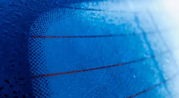 Gotas de agua sobre los **filamentos transversales de la luneta trasera** de un coche, creando un patrón abstracto azul.