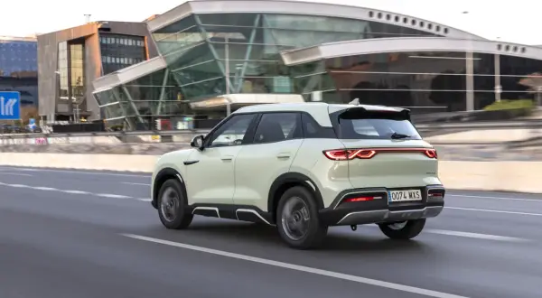 Jasny, nowoczesny BYD atto 2 jedzie po drodze, mijając futurystyczny budynek.