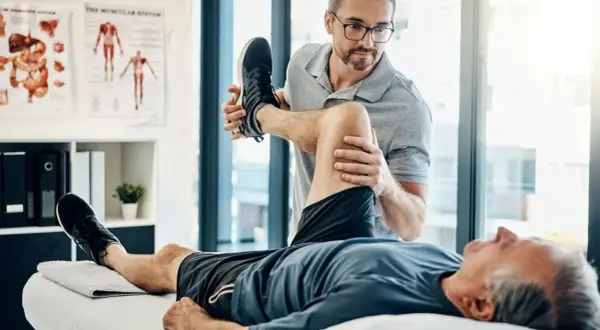 Fizjoterapeuta wykonuje ćwiczenia z pacjentem leżącym na kozetce.