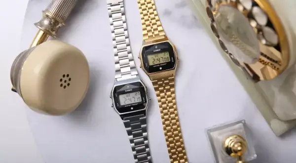 Dwa zegarki Casio, srebrny i złoty, obok retro telefonu. Idealne dla kobiet ceniących styl, często pojawiają się w rankingach luksusowe zegarki damskie ranking.