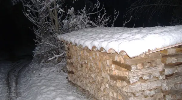 Une pile de bois peuplier chauffage sous la neige, prête pour l'hiver. Les branches enneigées d'un arbre se dressent à gauche.