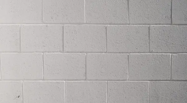 Mur de parpaings blancs, fraîchement peints au pistolet. La texture rugueuse des blocs est visible sous la couche de peinture uniforme.
