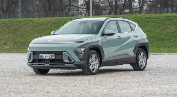 Nowy Hyundai Kona 1.6 benzyna w pastelowym kolorze, zaparkowany na żwirowym placu, gotowy na miejskie przygody.