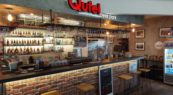 Wnętrze Qufel beer park z barem, butelkami piwa i menu.