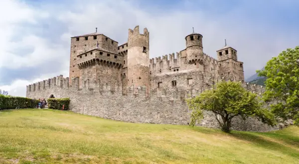Imponente castello medievale, uno dei borghi Valle d'Aosta più suggestivi, con torri merlate e mura in pietra su un prato verde.