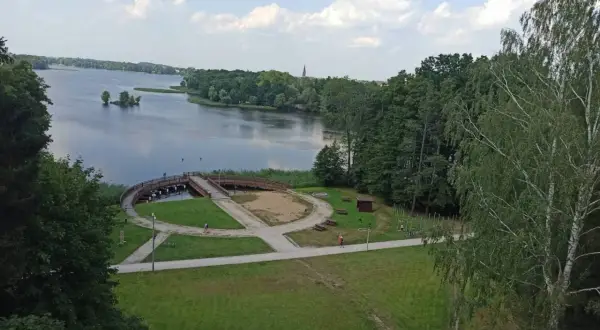 Malowniczy widok na jezioro i promenadę w Szczecinku. Widać ścieżki idealne na rowerowy spacer, mostek i zieleń.