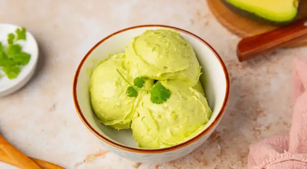 Un cremoso helado de aguacate, decorado con cilantro fresco, servido en un cuenco.