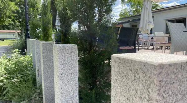 Granit-Palisaden setzen einen eleganten Akzent vor grüner Bepflanzung und laden zum Verweilen auf der Terrasse ein.