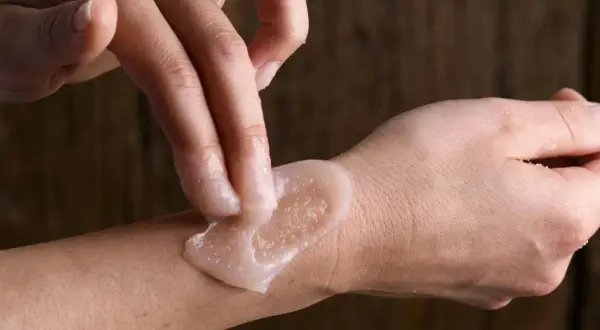 Mani che applicano scrub corpo sulla pelle, mostrando come si usa lo scrub corpo per una pelle liscia e luminosa.