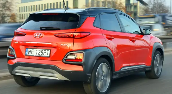 Czerwony Hyundai Kona 2025 z czarnym dachem pędzi po drodze, ukazując swoje nowoczesne tylne światła i masywne nadkola.