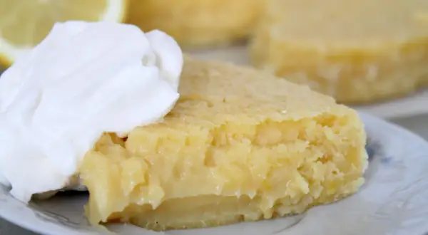 En bit kladdkaka med citron, toppad med vispad grädde. En perfekt citron kladdkaka för fikat.