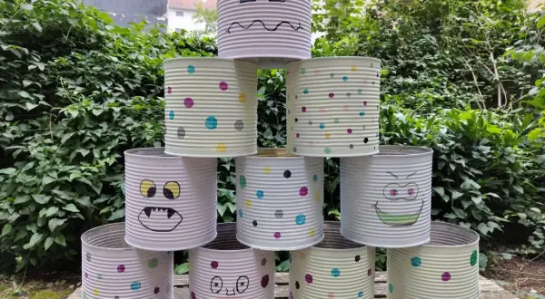Kreatives Recycling mit Kindern: Dosen-Monster-Turm im Garten. Bunte Punkte und lustige Gesichter machen aus alten Konserven ein Spiel.