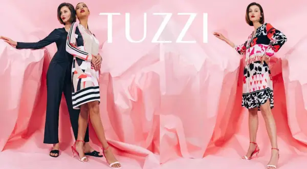 Eleganckie kobiety prezentują modne kreacje marki TUZZI na tle różowych, pofałdowanych tkanin.