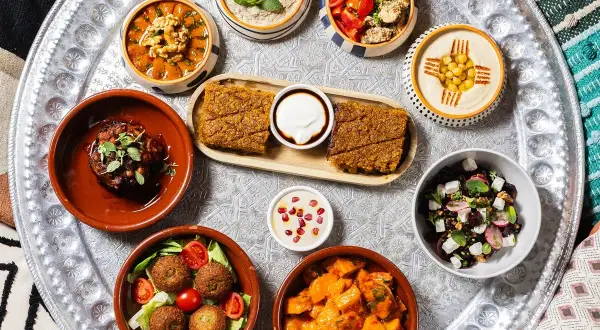 Un vassoio con diverse pietanze mediorientali, perfetto per scoprire dove mangiare a Milano. Hummus, falafel, insalate e spezzatini invitano a un viaggio di sapori.