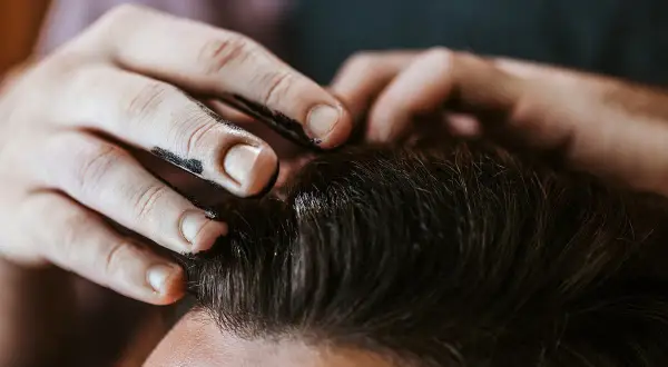 Main d'un coiffeur appliquant du gel ou de la cire sur les cheveux d'un client pour un coiffage parfait.