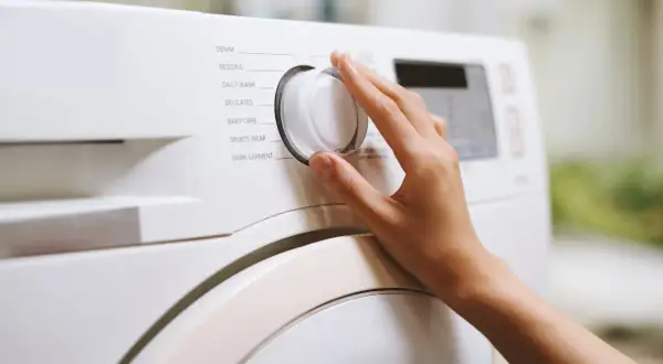 Dłoń kręci pokrętłem pralki, wybierając program "Bedding". Zastanawiasz się, w jakiej temperaturze prać pościel z kory? Sprawdź instrukcję pralki.