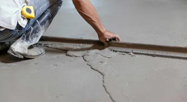 Obrero usa regla para nivelar suelo con tableros de cemento fresco.