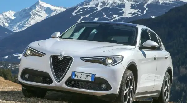 Białe Alfa Romeo Stelvio na tle ośnieżonych gór. Wiele pozytywnych alfa romeo stelvio opinie potwierdza jego wszechstronność.