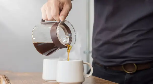 Versando caffè da una caraffa in due tazze. La scelta del caffè giusto è fondamentale per una macchina caffè americano.