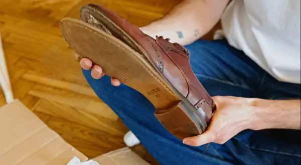 Une personne examine une chaussure en cuir marron, montrant l'usure de la semelle.