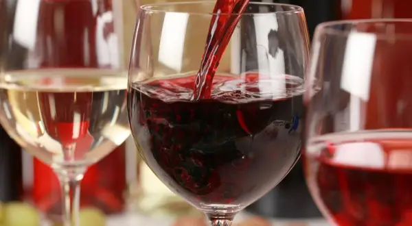 Czerwone wino nalewane do kieliszka, obok białe wino i butelki. Zastanawiasz się, ile kalorii ma wino?