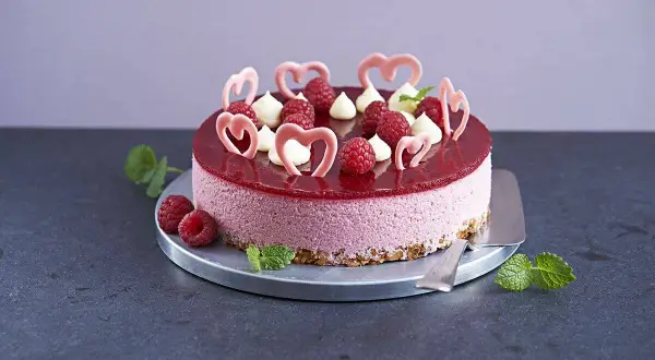 En vacker hallonmousse tårta med färska hallon, vita gräddtoppar och rosa hjärtdekorationer. Perfekt för ett speciellt tillfälle!