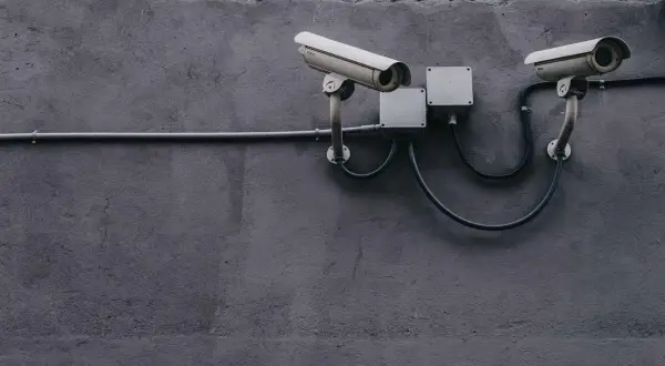 Dwie kamery monitoringu na szarej ścianie, podłączone do puszek elektrycznych. Zapewniają bezpieczeństwo i monitoring w domu.