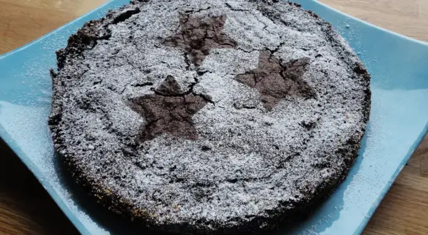 En härlig glutenfri kladdkaka med stjärnmönster av florsocker på en blå tallrik.