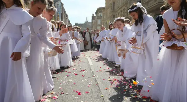 Dziewczynki w bieli sypią płatki kwiatów na ulicy. To piękny widok podczas procesji Bożego Ciała, święta upamiętniającego Ostatnią Wieczerzę.