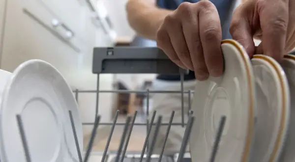 Ręce wkładają talerze do zmywarki Siemens. Mam nadzieję, że nie pojawi się błąd E24.