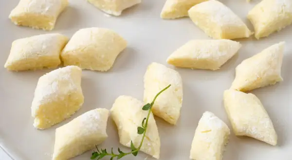 Kopytka z przepisu babci, delikatne i puszyste, posypane mąką, leżą na talerzu.