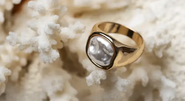 Anillo de oro amarillo con perla irregular sobre coral blanco. La diferencia entre oro blanco y oro amarillo es evidente en su brillo.