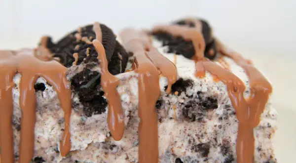 En bit krämig oreo cheesecake med chokladsås som rinner ner.