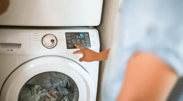 Mano che seleziona "Warm" sul pannello di una lavatrice, per capire quanto consuma una lavatrice a 40 gradi.