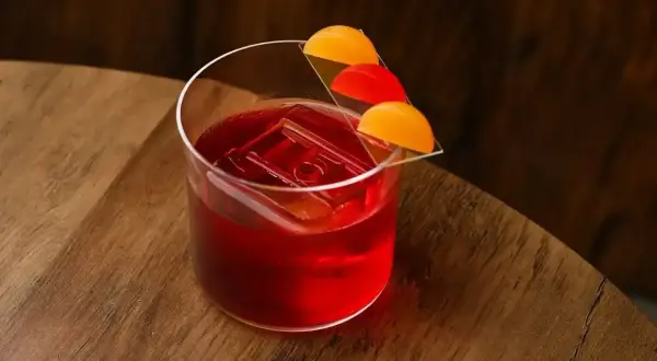 Elegancki negroni sklad z lodem i pomarańczową dekoracją na drewnianym blacie.