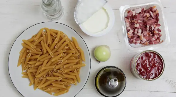 Penne, boczek, śmietana, cebula, oliwa, pomidory z puszki na białym tle.