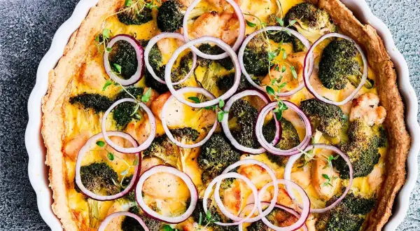 En gyllene vegansk paj med broccoli, kycklingbitar och rödlök, toppad med färska örter.