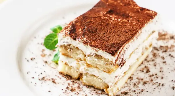 Une part de tiramisu mascarpone, aérienne et gourmande, saupoudrée de cacao, avec une touche de menthe fraîche.