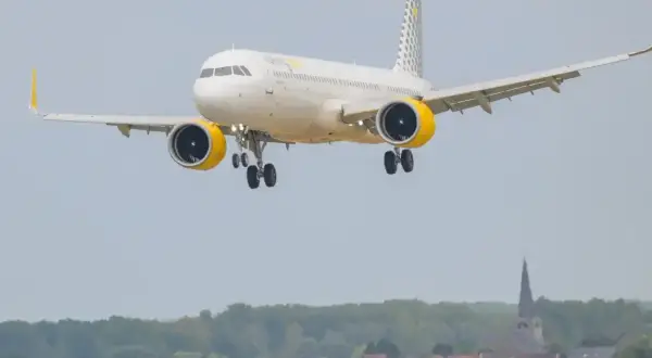 Samolot hiszpańskich linii lotniczych Vueling z żółtymi gondolami silników zbliża się do lądowania nad malowniczą miejscowością.