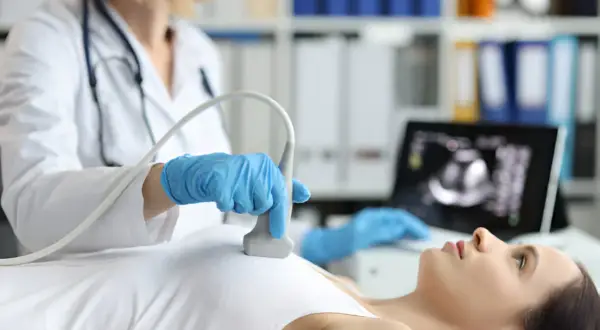Lekarka wykonuje badanie USG piersi, by wyjaśnić wątpliwości po mammografii. Obraz z monitora pokazuje szczegóły.