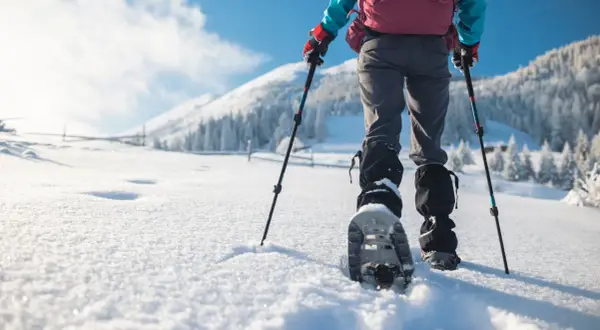 Randonnée en raquettes dans un paysage enneigé. Une personne avance dans la poudreuse, bâtons à la main, profitant des sports neige.