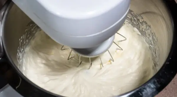 Mieszadło robota kuchennego ubija puszysty krem z ricotty do ciasta.