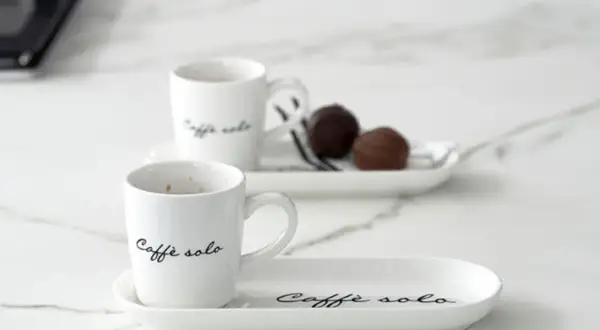 Eleganckie filiżanki z napisem "Caffè solo" i czekoladki na talerzykach. Idealny sposób, jak podawać kawę gościom.