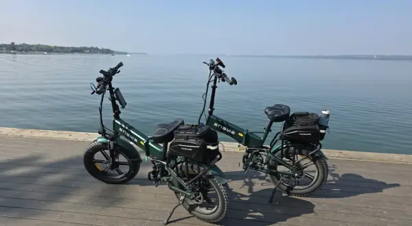 Dwa zielone rowery elektryczne z sakwami, gotowe na wyprawę z zasięgiem 200 km nad spokojną wodą.