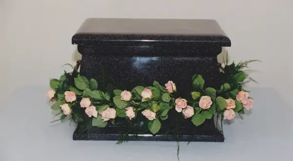 Czarna, kamienna urna ozdobiona girlandą z różowych różyczek i zieleni. Piękne kwiaty na trumnę, symbolizujące pamięć i miłość.