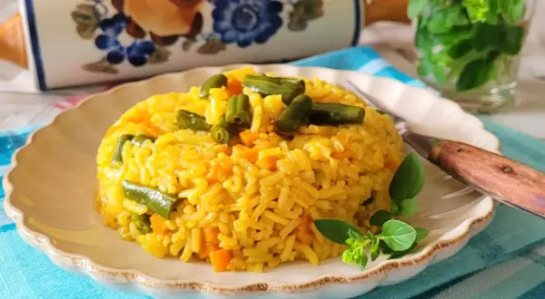 Ryż z curry, marchewką i fasolką szparagową na talerzu, ozdobiony ziołami.