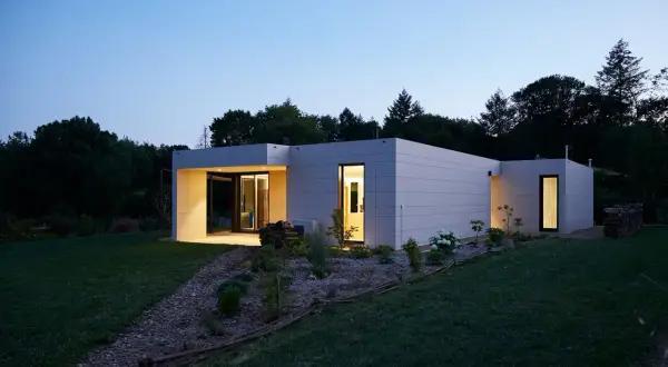 Modernos modelos de casas unifamiliares con fachadas de baldosas grises, iluminadas al anochecer.
