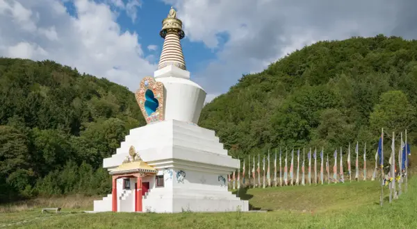 Biała stupa, miejsce, gdzie wyznaje się buddyzm, otoczona lasem i ozdobiona kolorowymi flagami modlitewnymi.